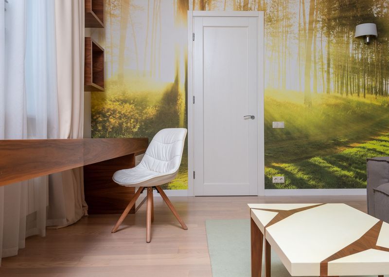 Home office with a sunlit forest wall mural around a white door, a walnut desk and a white swivel chair