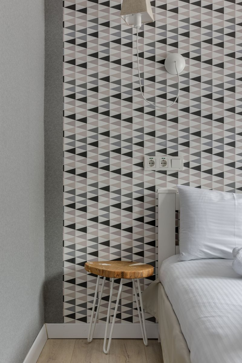 Bedroom feature strip of black, gray and white triangle-pattern wallpaper beside a white bed and a wooden stool