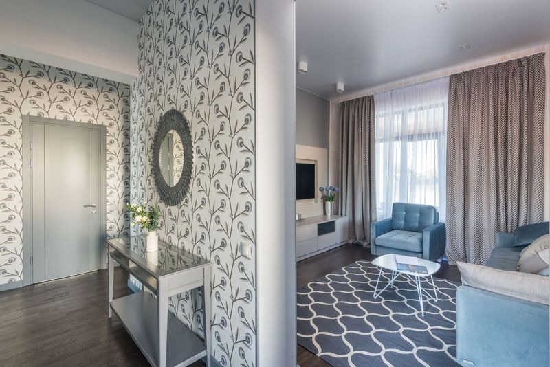 Entry hallway with a gray botanical-print wallpaper, a round mirror and a console table opening into a bright living room